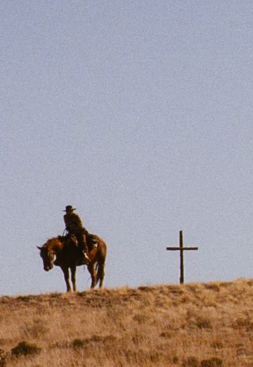 man on a horse standing to the left of a cross grave marker.